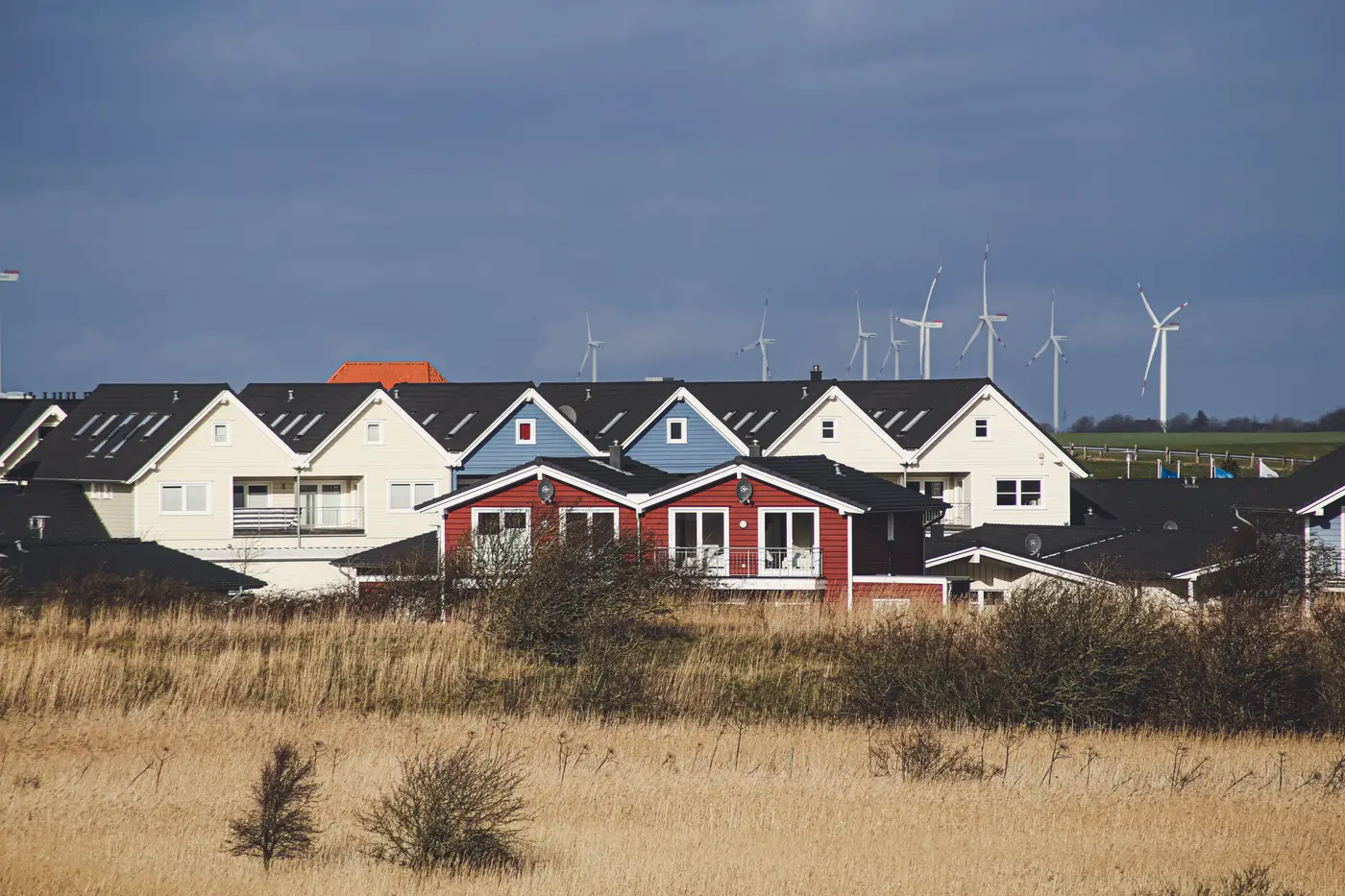 Village houses with wind turbines visible on the hillside and horizon behind them